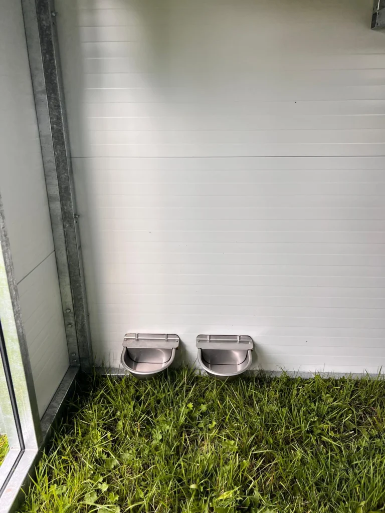 Poidła dla kur przykręcone na ścianie w dużym mobilnym kurniku